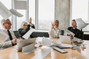 Group of happy coworkers celebrating a successful meeting, throwing papers and clapping in a modern office.