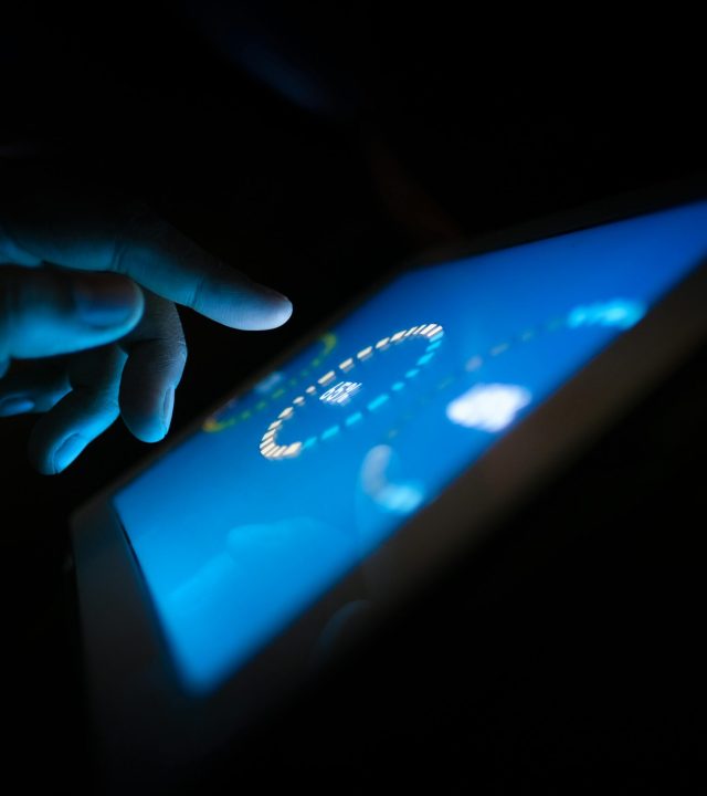 Close-up of a hand interacting with a glowing touchscreen in a dark setting, highlighting technology use.