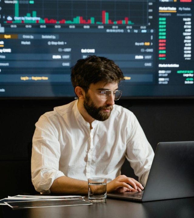 pexels-photo-7567434-7567434 Professional analyzing stock market trends using laptop and digital display in modern office.