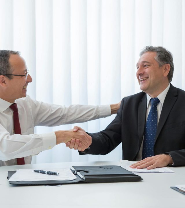 Two businessmen in a bright office seal a deal with a handshake, conveying agreement and cooperation.